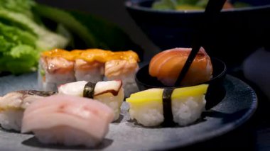 Nigiri, sashimi ve tamago 'yu da içeren beyaz bir tabak suşi, parlak ve hatta aydınlık arka planda siyah bir zemine karşı sorunsuzca döner. Yüksek kalite 4k görüntü