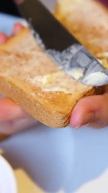 Çavdar ekmeğine tereyağı sürmüş bir kadın bıçakla. Bir parça ekmeğe kremalı tereyağı süren bir insan. Erkek ellerinin mutfakta ekmeğe tereyağı sürmesini, yavaş çekimde. Yüksek kalite