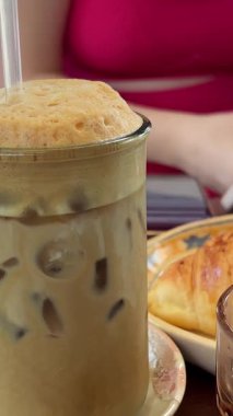 Camda cappuccino karıştıran dikey videolu kız. Güzel fincanda kahve ve milkshake. Köpüklü kahve. Latte yapma süreci. Manikür karıştırıcı cappuccino ile yakın plan kadın eli..