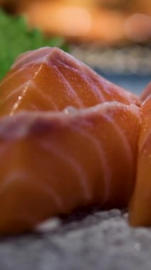 Seramik tabaktan taze somon ve ton balıklı sashimi dilimleri, salatalık ve wasabi ile süslenmiş, parlak stüdyo ışıkları altında ve siyah arka planda. Yüksek kalite 4k görüntü