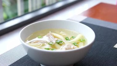 Bambu masa paspasının üzerindeki beyaz kaseye doğranmış yeşillik serpiştirilmiş erişteli ev yapımı temiz tavuk çorbası, yakın çekim. Erişte çorbasına otlar serpin.