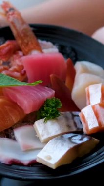 Canlı bir tabak somon, ton balığı, deniz tarağı sashimi ve somon yumurtası parlak stüdyo ışıkları altında pürüzsüz bir şekilde döner, taze deniz ürünleri ve süslemeler vurgulanır. Yüksek kalite 4k görüntü