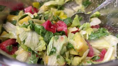 Çatal kullanarak kadın ellerini kapat ve cam kaseden renkli bir salatayı mutfak masasındaki mavi bir tabağa servis et, sağlıklı beslenme alışkanlıklarını teşvik et. Üst manzara, genel giderler. Yüksek kalite 4k görüntü