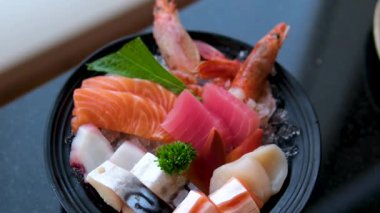 Suşi, somon, ton balığı, deniz tarağı ve somon yumurtası gibi çeşitli suşiler, garnitürlerle dolu bir tabakta sunuluyor, stüdyo ışıkları altında düzgün bir şekilde dönüyor. Yüksek kalite 4k görüntü