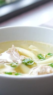 Bambu masa paspasının üzerindeki beyaz kaseye doğranmış yeşillik serpiştirilmiş erişteli ev yapımı temiz tavuk çorbası, yakın çekim. Erişte çorbasına otlar serpin.