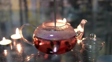 Ve mum ışığında koyu bir arka planda cam çaydanlıkta bir kaşıkla kırmızı amber çayı karıştır. Kız çay seremonisine hazırlanıyor. Mum ve tütsü yakar. Alçak ahşap bir masada çay içerken 