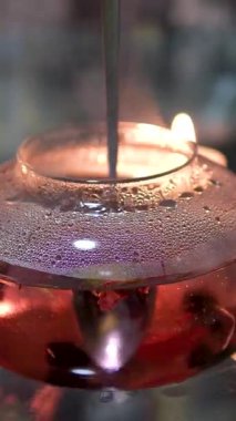 Ve mum ışığında koyu bir arka planda cam çaydanlıkta bir kaşıkla kırmızı amber çayı karıştır. Kız çay seremonisine hazırlanıyor. Mum ve tütsü yakar. Alçak ahşap bir masada çay içerken 