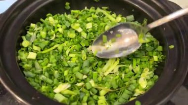 Ev yemeği dikkatlice beyaz kesme tahtasında yeşil soğan doğrarken hafif kör bıçakla, günlük mutfak ortamında ev yapımı yemek için basit malzemeler hazırlarken. Yüksek kalite 4k görüntü