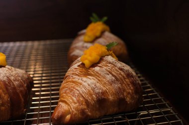  Modern bir kafe fırınında sergilenen çırpılmış kremayla dolu ve üzeri dilimlenmiş mangolarla kaplı bir tepsi kruvasan. Yüksek kalite fotoğraf