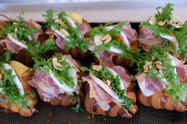 Kruvasan sandviçi, yanında Serrano jambonu ve roka yaprakları. Ellerini kruvasanın üstüne koy, sağlıklı yiyecekler. Yüksek kalite 4k görüntü