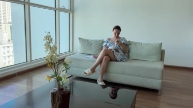 Güzel esmer kadın, ayakları masanın üzerinde beyaz koltukta otururken bir kitap okuyor, dikiz aynası 4k video. Yüksek kalite 4k görüntü