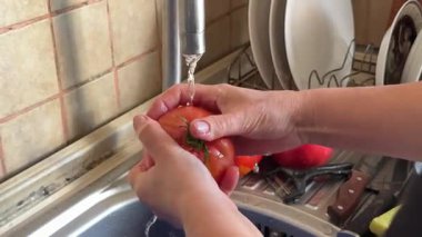 Mutfaktaki musluğun altında domates yıka. Mutfakta akan musluk suyunun altında pembe domatesler yıka. Yüksek kalite 4k görüntü