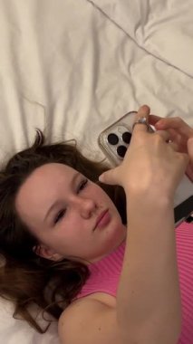 Bir kadın, sakin ve rahat bir ortamda telefonunu karıştırarak yatakta uzanıyor. Yüksek kalite 4k görüntü