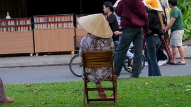 Vietnam şapkalı kadınlar dışarıda sandalyede oturmuş turistlerin yürüyüşünü ve Hoi An 'dan geçen bisikletleri izliyorlar.