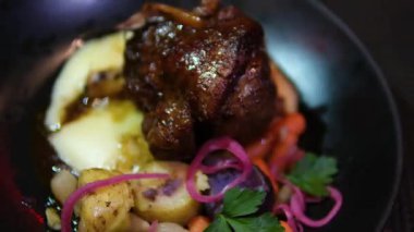 Bitmiş bir tabağın yakın çekimi. Kök sebzeli ve adaçaylı dana eti. Siyah tabakta patates ve salata ile dana bacağı, restoranda üç çeşit öğle yemeği.