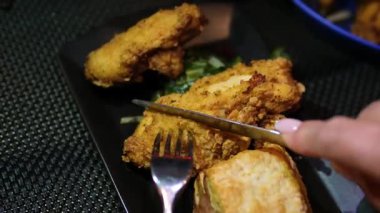 Restoranda çatal ve bıçakla yenen siyah bir tabakta kızarmış kanatlar. Yüksek kalite 4k görüntü