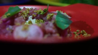 Delicate fish tartare made of raw minced fish beautifully plated on a red dish with radish greens and pistachios perfect for gourmet food photography culinary videos and restaurant menus.