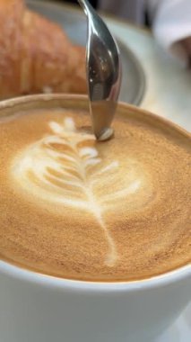 Bardakta karıştırılmış latte. El, uzun saplı kaşıkla büyük bardakta latte ile şeker karıştırır. Bir kafede latte içerken yakın çekim. Latte Latte kruvasan kaşığını karıştır.