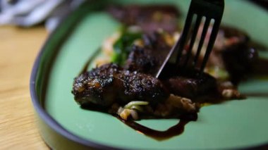 Buğday lapasında orta pişmiş biftek, ıspanaklı, yeşil tabakta tereyağı, çatal ve bıçakla yenmiş..