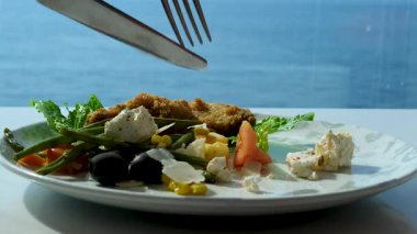 Plaj lokantasında hasır şapkalı, tropikal öğle yemeği yiyen bir kadın. Okyanus manzaralı açık hava yemekleri, canlı kokteyller ve taze yemekler. Rahatlama ve rahatlama konsepti. Yüksek kalite 4k