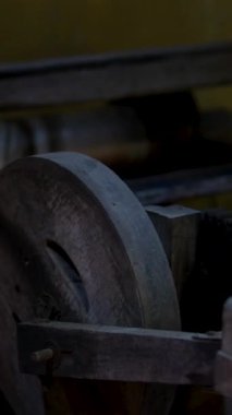 Loş aydınlatılmış bir atölyede, eskimiş ahşap bir tekerlek, eskimiş ahşap bir atmosfer yaratan eski ahşap kalaslarla çevrili, sağlam bir çerçeve üzerinde duruyor. Yüksek kalite 4k görüntü