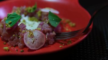 Delicate fish tartare made of raw minced fish beautifully plated on a red dish with radish greens and pistachios perfect for gourmet food photography culinary videos and restaurant menus.