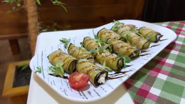 Keskin keçi peyniriyle doldurulmuş ızgara patlıcan ruloları gevrek ceviz ve mis kokulu otlarla kaplı, ahşap yüzeyde dinleniyor. Yüksek kalite 4k görüntü