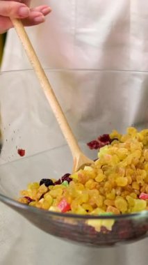 Şekerli meyve karışımı beyaz arkaplanı açar. Kadınların elleri kurumuş meyvelerle üzümleri karıştırır ve konyağa batırır.