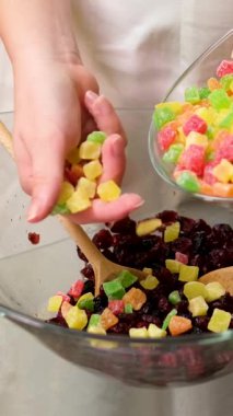 Şekerli meyve karışımı beyaz arkaplanı açar. Kadınların elleri kurumuş meyvelerle üzümleri karıştırır ve konyağa batırır.