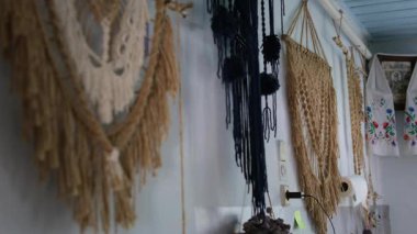 Seramik kireçlenmiş beyaz kireçlenmiş bir duvarın yanında duran eski soba, makrome ve antika bir saatle dekore edilmiş, rahat bir kırsal atmosfer yaratıyor..