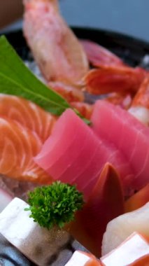 Suşi, somon, ton balığı, deniz tarağı ve somon yumurtası gibi çeşitli suşiler, garnitürlerle dolu bir tabakta sunuluyor, stüdyo ışıkları altında düzgün bir şekilde dönüyor. Yüksek kalite 4k görüntü