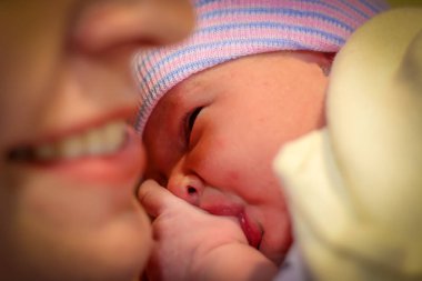Yeni doğmuş bir bebek annesinin göğsünde yatarken parmağını emiyor.