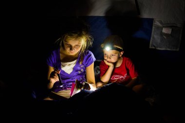 Çadırda bir kız ve bir oğlan karanlıkta kitap okuyor.