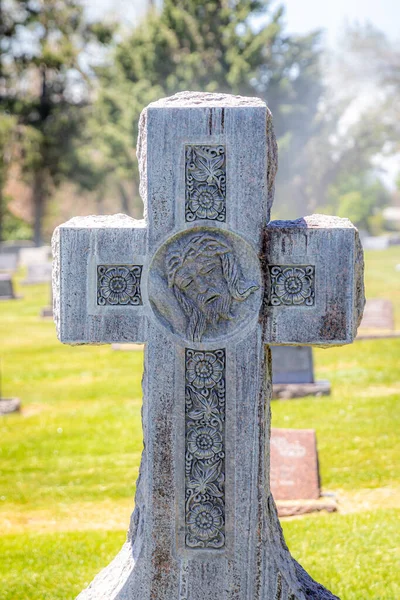 A large religious cross-shaped stone headstone with the face of Jesus Christ at the intersection at a cemetery