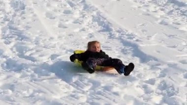 Küçük kız kışın tepeden aşağıya kar kızağı sürüyor.