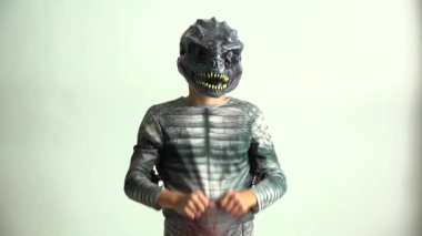 Dinozor kostümlü küçük çocuk elinde bir Jack O Fener Şeker Kovası tutuyor.