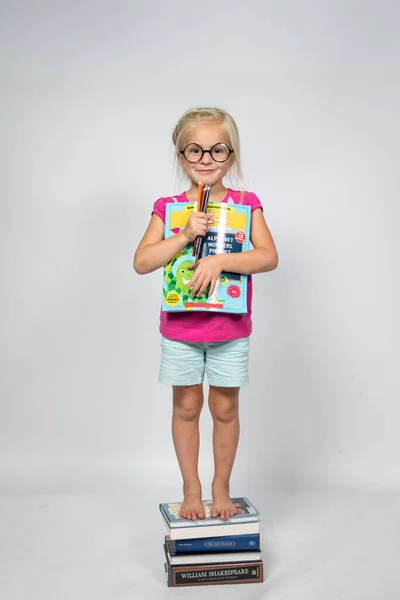 Cute Little Girl Standing on Books while holding onto school book and pencils