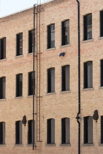 stock image The exterior side of a four story brown brick building with a fire emergency escape ladder