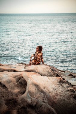 African woman watching the sunset, with curly hair and dressed in a kaftan, in silver on stones