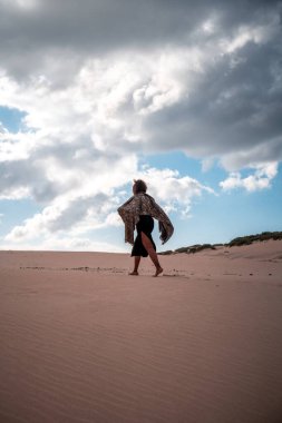 African woman with scarf walking in the dunes.