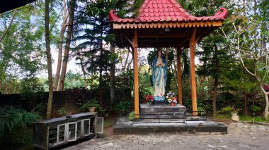 Bakire Meryem heykeli arka planda ağaçlarla kaplı bir gölgelik altında, Jatiningsih Maria Mağarası 'nda, Jogjakarta, Katoliklerin dua ettiği yerde, Tanrı' ya şükredin.