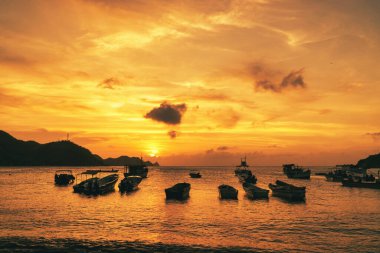 Denizde gün batımının ve kıyıda teknelerin olduğu manzara. Taganga Sahili. Santa Marta, Kolombiya. 