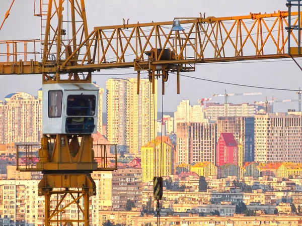 İnşaat vinçleri tamamlanmamış konut binasının üzerinde güneş ışığına karşı. Konut inşaatı, şehirdeki apartman bloğu