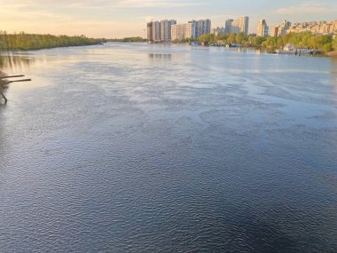Beautiful panoramic view of the city of Kyiv Dneper River at sunset on dark blue water with glowing reflected rays of the sun, copy-space. View of the deep river with the buildings in the background.
