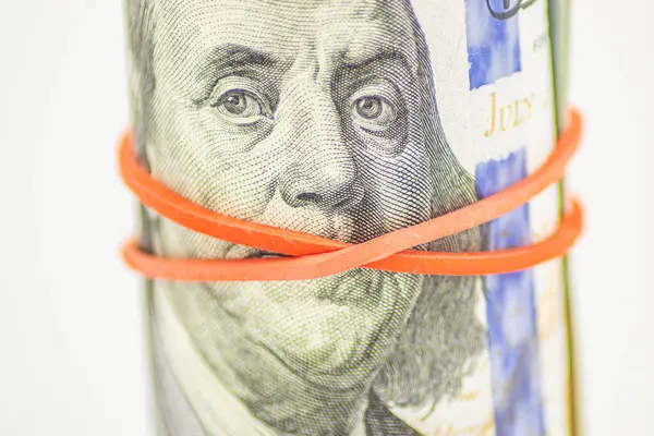 Concept of silent money. Red tape covers Franklin\'s mouth on the 100 bill. Bribery, money laundering, trafficking. Rolled up money isolated on white background. Dollar roll wrapped with red ribbon