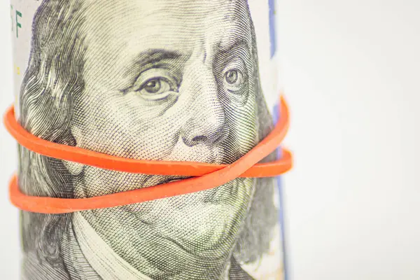 Concept of silent money. Red tape covers Franklin\'s mouth on the 100 bill. Bribery, money laundering, trafficking. Rolled up money isolated on white background. Dollar roll wrapped with red ribbon