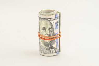 Beyaz arka planda izole edilmiş 100 dolarlık banknotlar. Beyaz arka planda izole edilmiş yuvarlanmış para. Beyaz arka planda izole edilmiş dolar. Kırmızı kurdeleyle sarılmış dolar rulosu.
