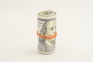 Beyaz arka planda izole edilmiş 100 dolarlık banknotlar. Beyaz arka planda izole edilmiş yuvarlanmış para. Beyaz arka planda izole edilmiş dolar. Kırmızı kurdeleyle sarılmış dolar rulosu.