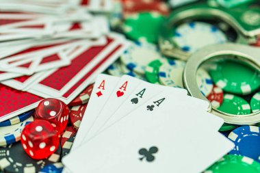 Poker masasında kelepçe ve silah. Kumarhane suçu konsepti, yeraltı kumarhaneleri. Yasadışı oyunlar, kumar konsepti. Masada, zarlı, paralı ve fişli iskambil kağıtları var. Kumarhane konsepti, oyunlar