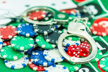 Poker masasında kelepçe ve silah. Kumarhane suçu konsepti, yeraltı kumarhaneleri. Yasadışı oyunlar, kumar konsepti. Masada, zarlı, paralı ve fişli iskambil kağıtları var. Kumarhane konsepti, oyunlar